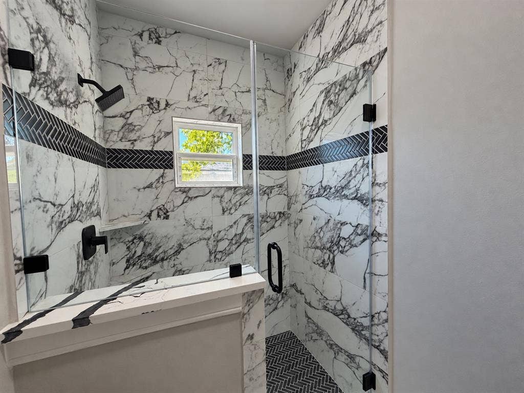 707 N Blanche Street, Terrell, TX 75160 Walk-in shower featuring large-format patterned wall tile, a contrasting herringbone accent border, a glass enclosure, a built-in stone-top ledge, and matte black plumbing fixtures