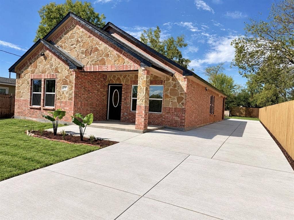 707 N Blanche Street, Terrell, TX 75160 Single-story exterior featuring a brick and stone facade, covered front entryway, expansive concrete driveway, and wooden privacy fencing