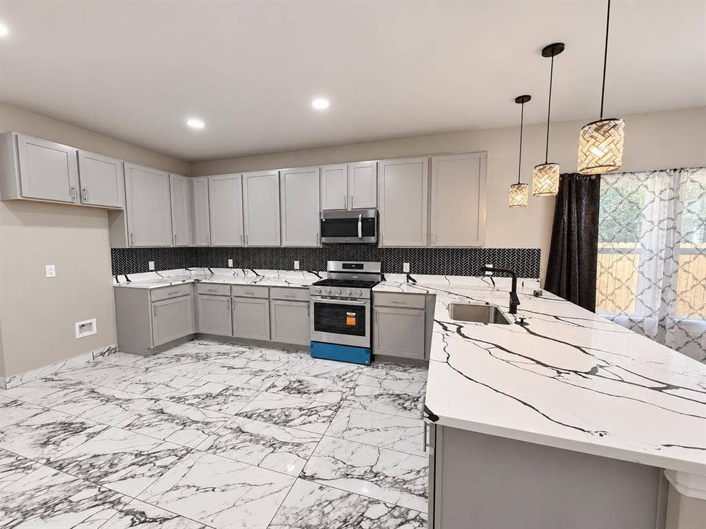 707 N Blanche Street, Terrell, TX 75160 Kitchen featuring light gray cabinetry, large-format veined tile flooring, solid surface countertops with contrasting veining, a decorative geometric tile backsplash, and three suspended pendant lights