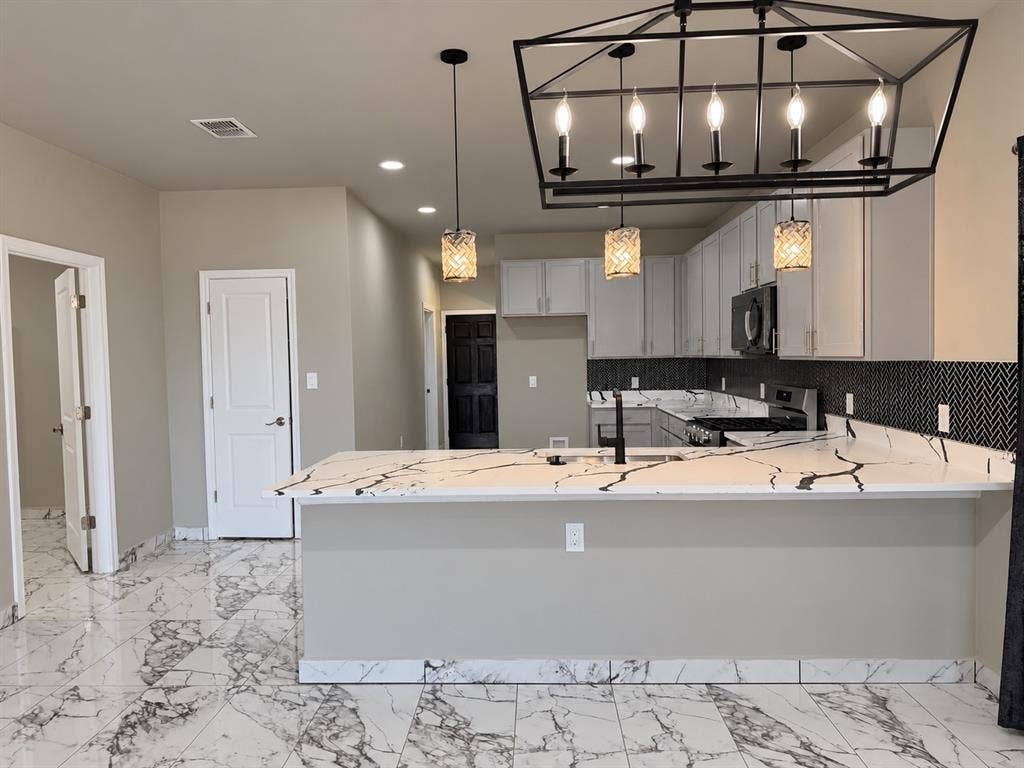 707 N Blanche Street, Terrell, TX 75160 Kitchen featuring stone-patterned tile flooring, a peninsula with stone-look countertop, herringbone-patterned tile backsplash, and decorative pendant and chandelier lighting