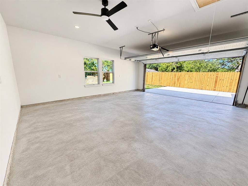 707 N Blanche Street, Terrell, TX 75160 Two-car garage featuring a smooth concrete floor, dual windows, matte black ceiling fan, and automated garage door opener