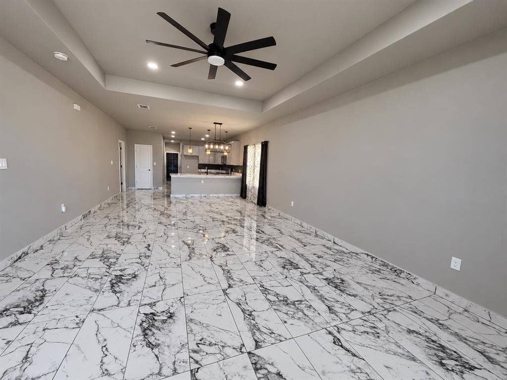 707 N Blanche Street, Terrell, TX 75160 Large open area featuring a tray ceiling, matte black multi-blade ceiling fan, recessed lighting, and polished stone-finish tile flooring