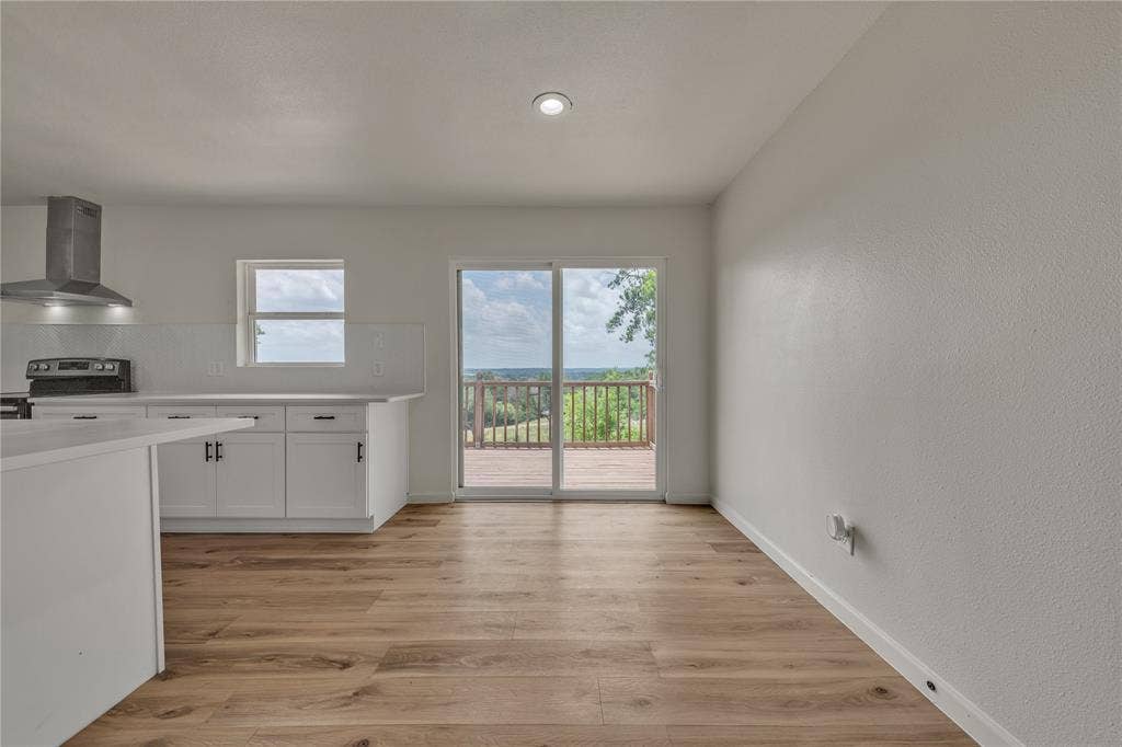 1719 Boot Hill Road, Granbury, TX 76049 Kitchen area featuring white cabinetry, a stainless steel range hood, wood-finish flooring, and sliding glass doors with exterior access