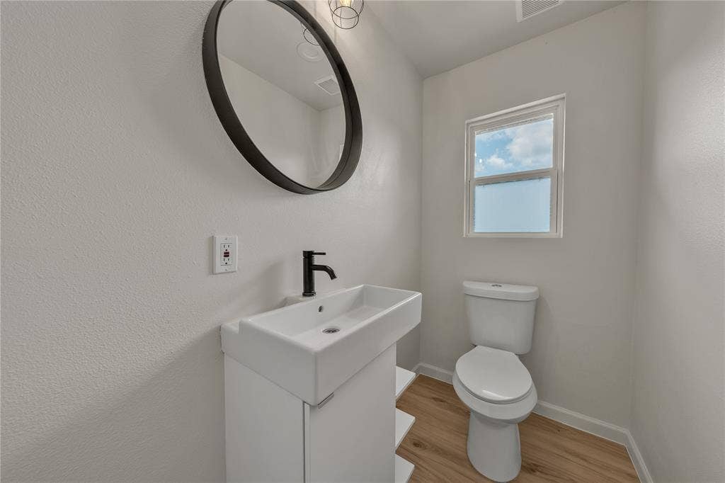 1719 Boot Hill Road, Granbury, TX 76049 Modern white pedestal vanity with matte black faucet, circular black-framed mirror, and wood-finish flooring