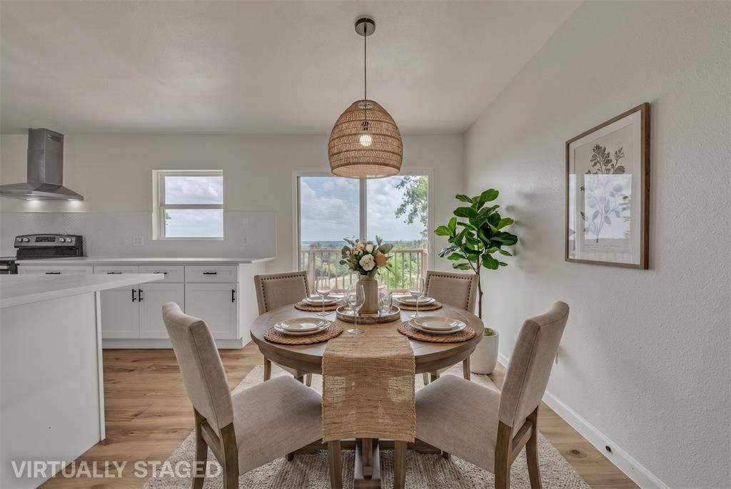 1719 Boot Hill Road, Granbury, TX 76049 Open-concept kitchen featuring white cabinetry, a stainless steel range hood, wood-finish flooring, and a glass sliding door with exterior scenery