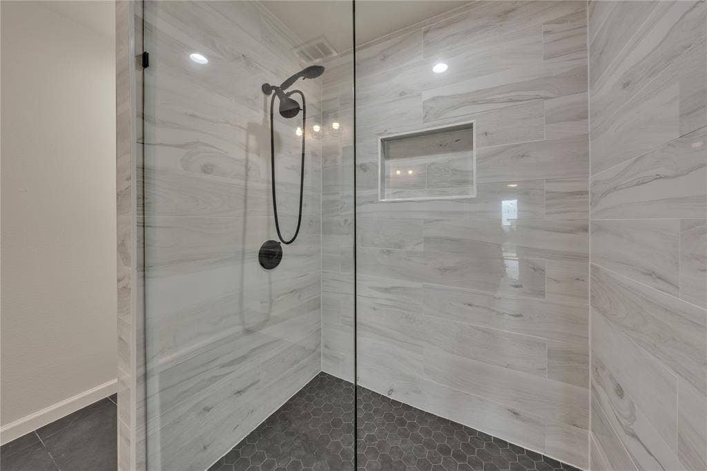 1719 Boot Hill Road, Granbury, TX 76049 Walk-in shower featuring large-format horizontal wall tile, hexagonal floor tile, matte black plumbing fixtures, glass enclosure, and a built-in recessed wall niche