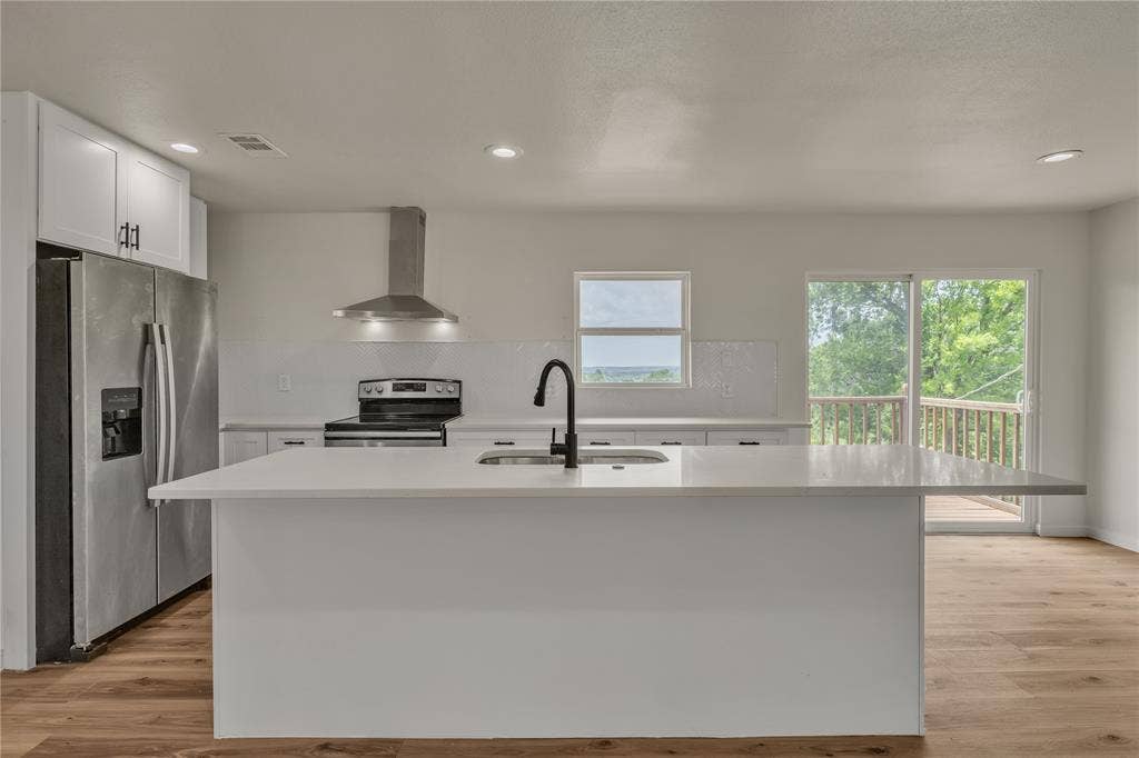 1719 Boot Hill Road, Granbury, TX 76049 Kitchen featuring a central island with a quartz countertop, stainless steel appliances, a stainless steel range hood, matte black faucet hardware, and wood-finish flooring