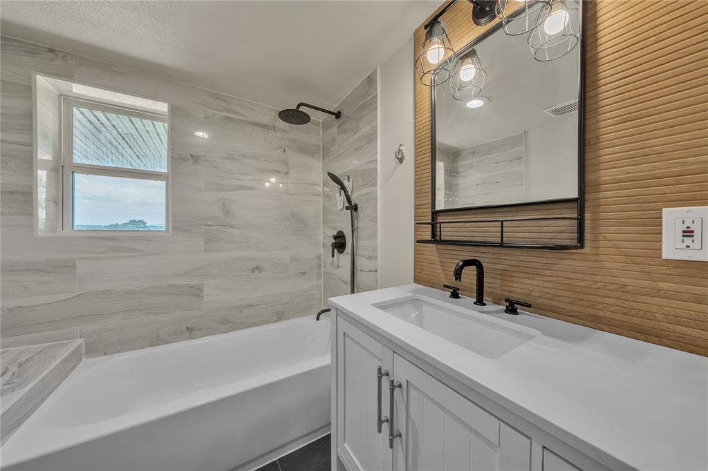 1719 Boot Hill Road, Granbury, TX 76049 Bathroom featuring a white vanity with a rectangular basin, quartz countertop, matte black plumbing fixtures, wood-slat accent wall, and a tiled shower surround