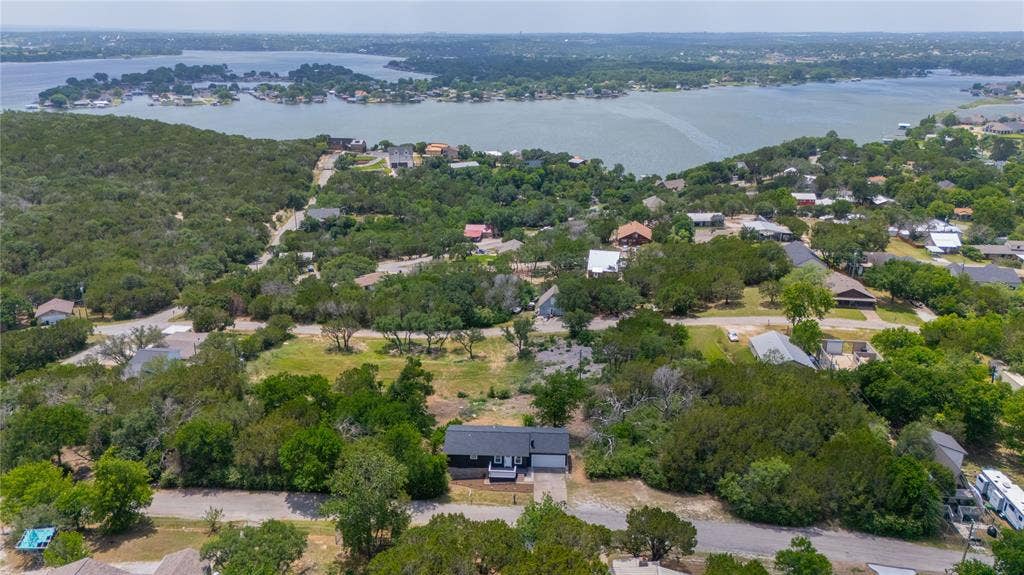 1719 Boot Hill Road, Granbury, TX 76049 Aerial perspective showcasing a single-story residence with a dark exterior, attached garage, paved driveway, and expansive natural landscape