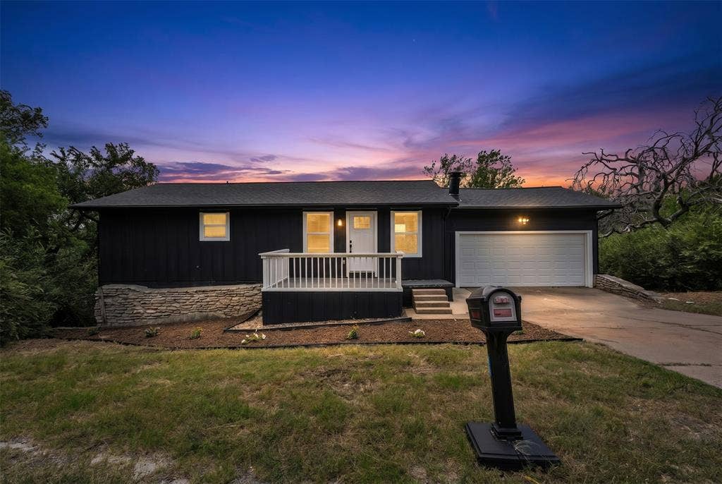 1719 Boot Hill Road, Granbury, TX 76049 Single-story exterior featuring dark vertical siding, stone foundation accents, a front porch with white railing, and an attached two-car garage