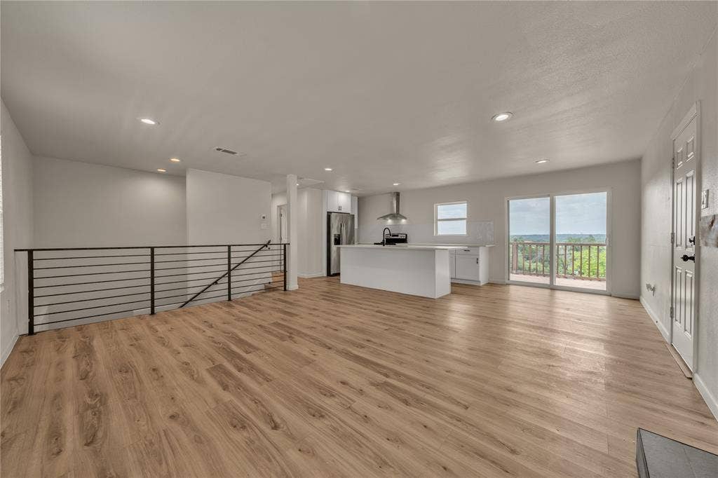 1719 Boot Hill Road, Granbury, TX 76049 Open-concept floor plan featuring wood-finish flooring, a kitchen island with stone-finish countertops, stainless steel appliances, recessed lighting, and a metal horizontal-rail staircase