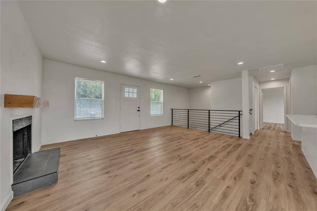 1719 Boot Hill Road, Granbury, TX 76049 Open-concept interior featuring wood-finish flooring, recessed lighting, a stone-surround fireplace with a timber mantel, and an industrial-style metal stair railing
