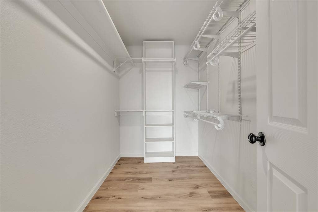 1719 Boot Hill Road, Granbury, TX 76049 Walk-in closet featuring wood-finish flooring, white-finish wall shelving, tiered vertical built-in shelving, and wire hanging rods