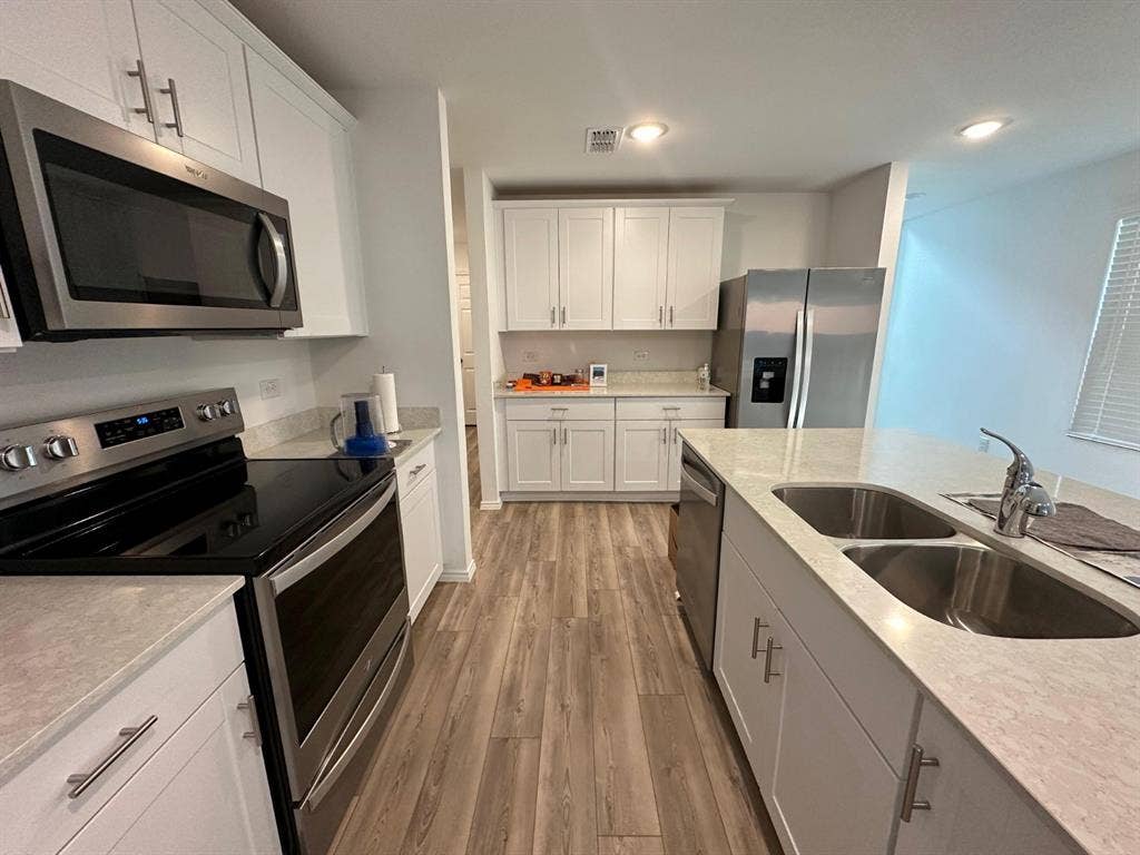 821 POPPY COVE Lane, Princeton, TX 75407 Kitchen featuring white Shaker-style cabinetry, stainless steel appliances, a central island with a double-basin sink, quartz countertops, and wood-finish flooring