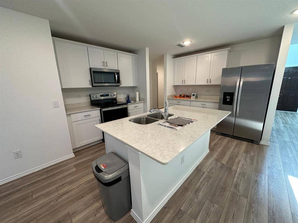 821 POPPY COVE Lane, Princeton, TX 75407 Kitchen featuring white shaker-style cabinetry, stone-finish countertops, stainless steel appliances, a center island with an integrated double-basin sink, and wood-finish flooring