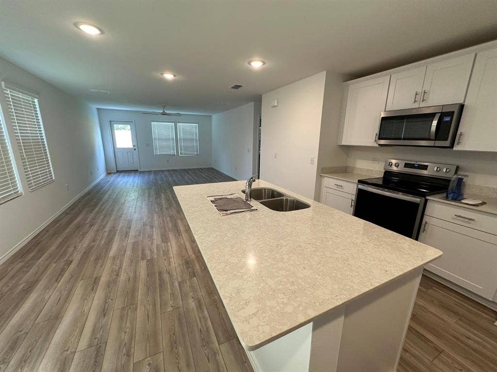 821 POPPY COVE Lane, Princeton, TX 75407 Kitchen featuring white cabinetry, a center island with a stone-composite countertop and stainless steel double-basin sink, and wood-finish flooring throughout
