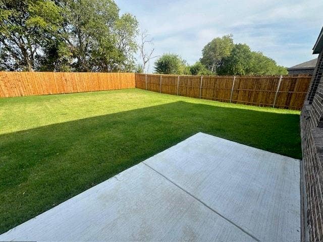 821 POPPY COVE Lane, Princeton, TX 75407 Rear exterior featuring a concrete patio, a level grass lawn, and a full-height wood perimeter fence