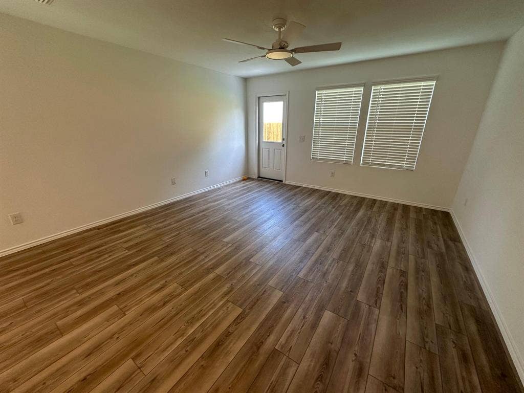 821 POPPY COVE Lane, Princeton, TX 75407 Interior room featuring wood-finish flooring, a ceiling fan with integrated lighting, dual windows with horizontal blinds, and a paneled exterior door