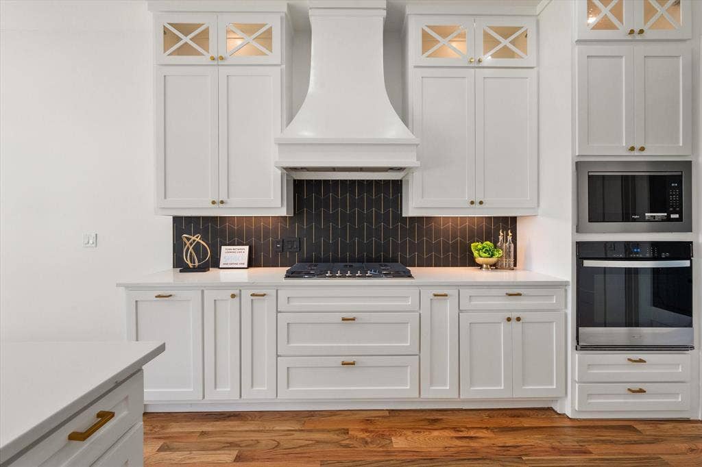 122 Yvonne Street, Red Oak, TX 75154 Custom designed hood and modern black/gold tiled backsplash and a 5 burner gas stove. Electric Whirlpool oven and built in microwave