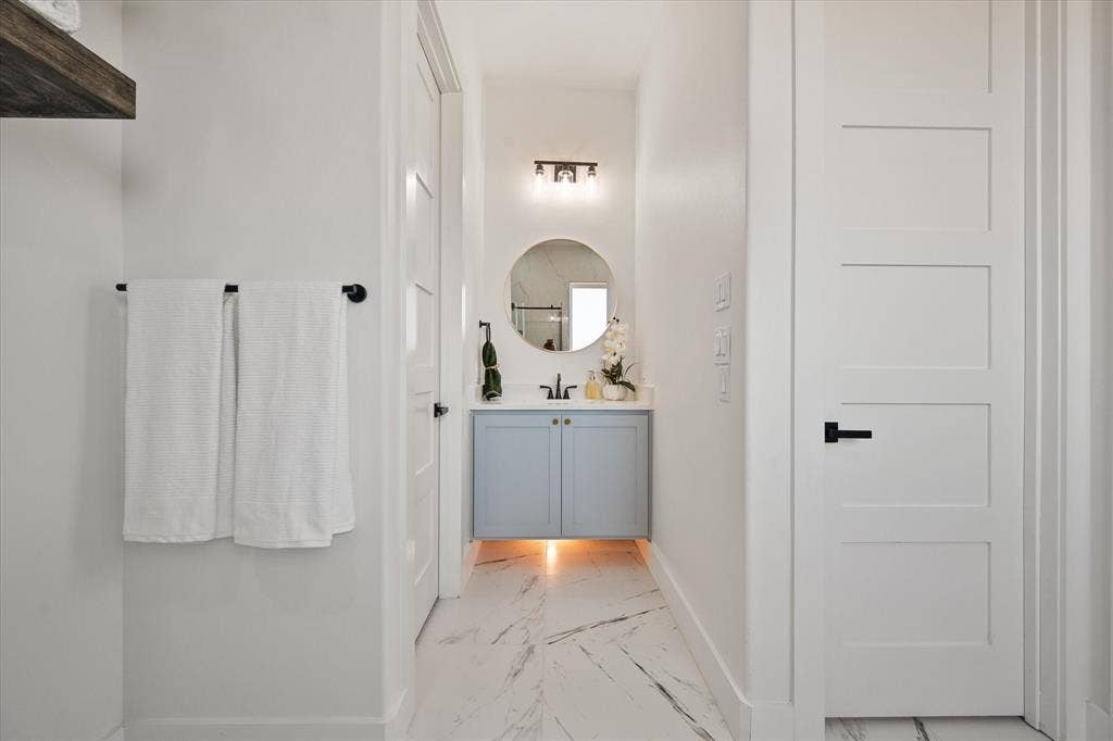 122 Yvonne Street, Red Oak, TX 75154 Mother in law ensuite bathroom with a floating vanity with cabinet and solid Quartz countertop, round mirror, three-light matte black vanity fixture, and large-format tile flooring with marble-finish veining