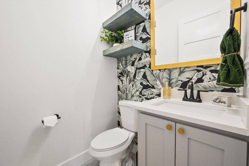 122 Yvonne Street, Red Oak, TX 75154 Hallway half bathroom with a shaker-style floating vanity with a Quartz countertop, matte black faucet, gold-toned hardware, and decorative botanical-patterned wallpaper