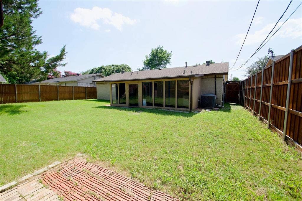 2708 N Avenue, Plano, TX 75074 Backyard featuring a red brick patio, sprawling grass lawn, floor-to-ceiling glass paneling, and perimeter wood fencing