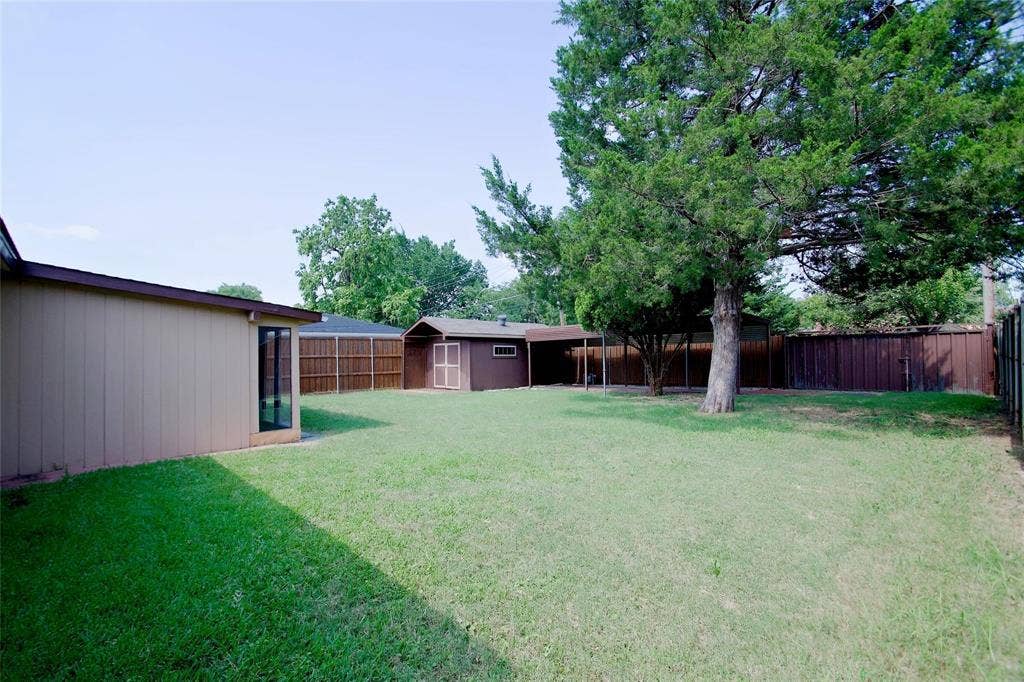 2708 N Avenue, Plano, TX 75074 Expansive backyard featuring a level lawn, mature shade trees, a detached storage structure, and perimeter wood fencing