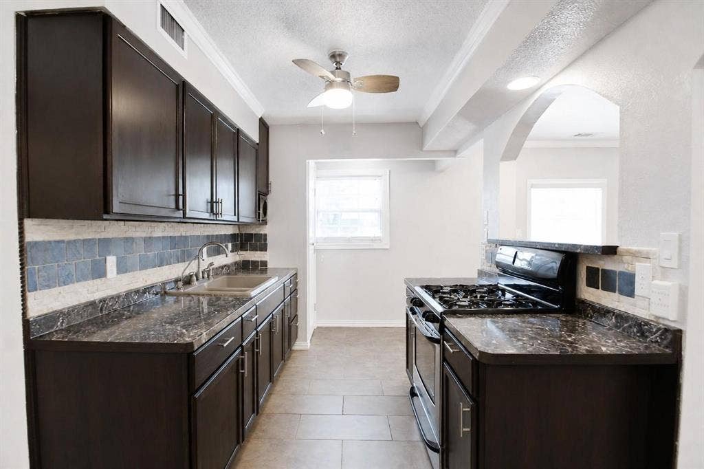 2708 N Avenue, Plano, TX 75074 Kitchen featuring dark-finish cabinetry, patterned stone-surface countertops, tile backsplash, tile flooring, and an arched architectural opening