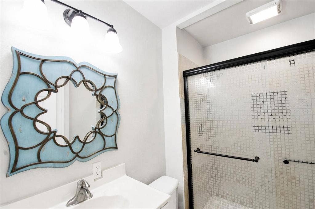 2708 N Avenue, Plano, TX 75074 Bathroom vanity featuring a solid surface countertop with integrated basin, three-light wall fixture, and walk-in shower with a black-framed sliding door