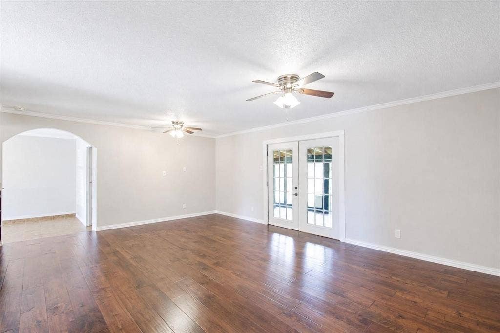 2708 N Avenue, Plano, TX 75074 Spacious interior featuring wood-finish flooring, dual ceiling fans with integrated lighting, a structural arched doorway, and double-paned glass French doors