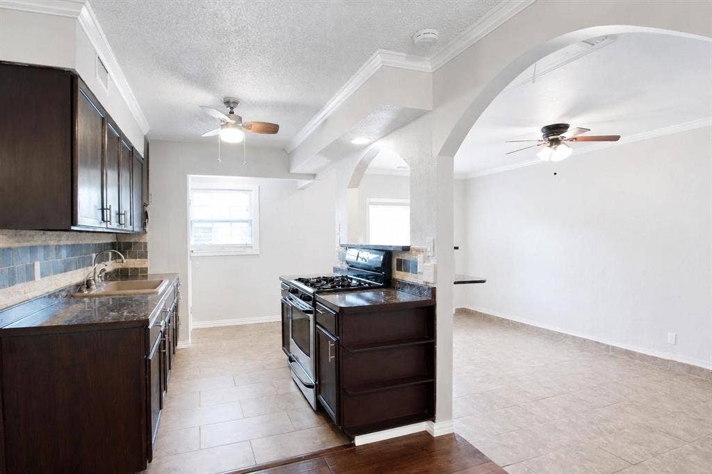 2708 N Avenue, Plano, TX 75074 Kitchen featuring dark cabinetry, stone-finish countertops, tiled backsplash, stainless steel gas range, and arched architectural detailing