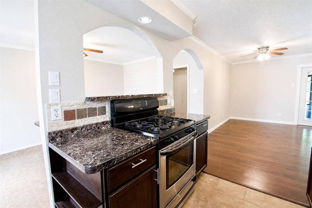 2708 N Avenue, Plano, TX 75074 Kitchen featuring dark wood-finish cabinetry, a gas range, stone-patterned countertops, decorative tile backsplash, and arched wall openings