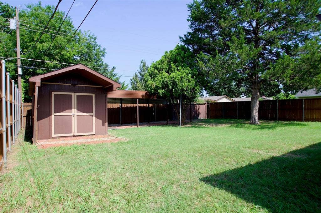 2708 N Avenue, Plano, TX 75074 Rear yard featuring a manicured lawn, detached storage shed, covered outdoor structure, wood-style perimeter fencing, and mature trees