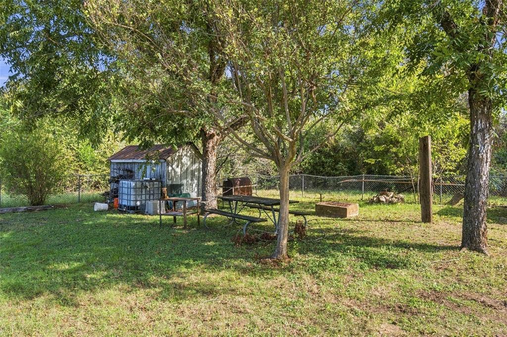 1703 Arra Street, Waco, TX 76704 Spacious backyard featuring mature trees, a detached storage structure, and chain-link perimeter fencing