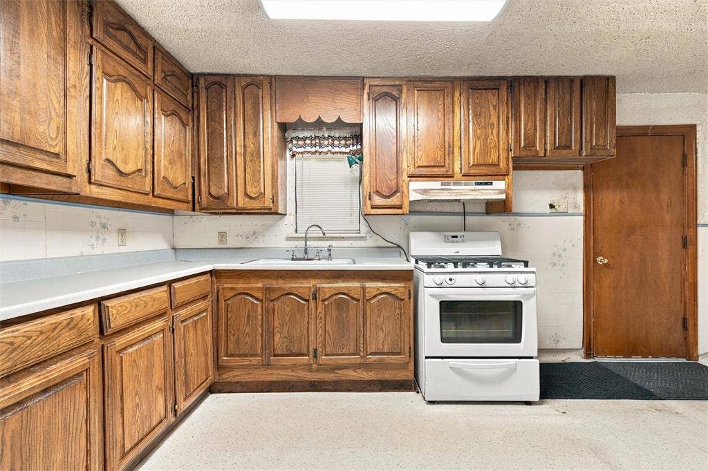 1703 Arra Street, Waco, TX 76704 Kitchen featuring raised-panel wood cabinetry, white countertops, integrated sink with metal faucet, and white freestanding gas range