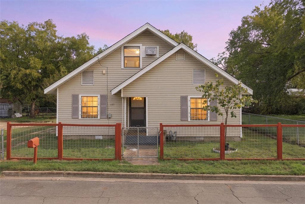 1703 Arra Street, Waco, TX 76704 Exterior featuring light-toned horizontal siding, a gabled roofline, symmetrical shuttered windows, and a fenced front yard with a metal gate