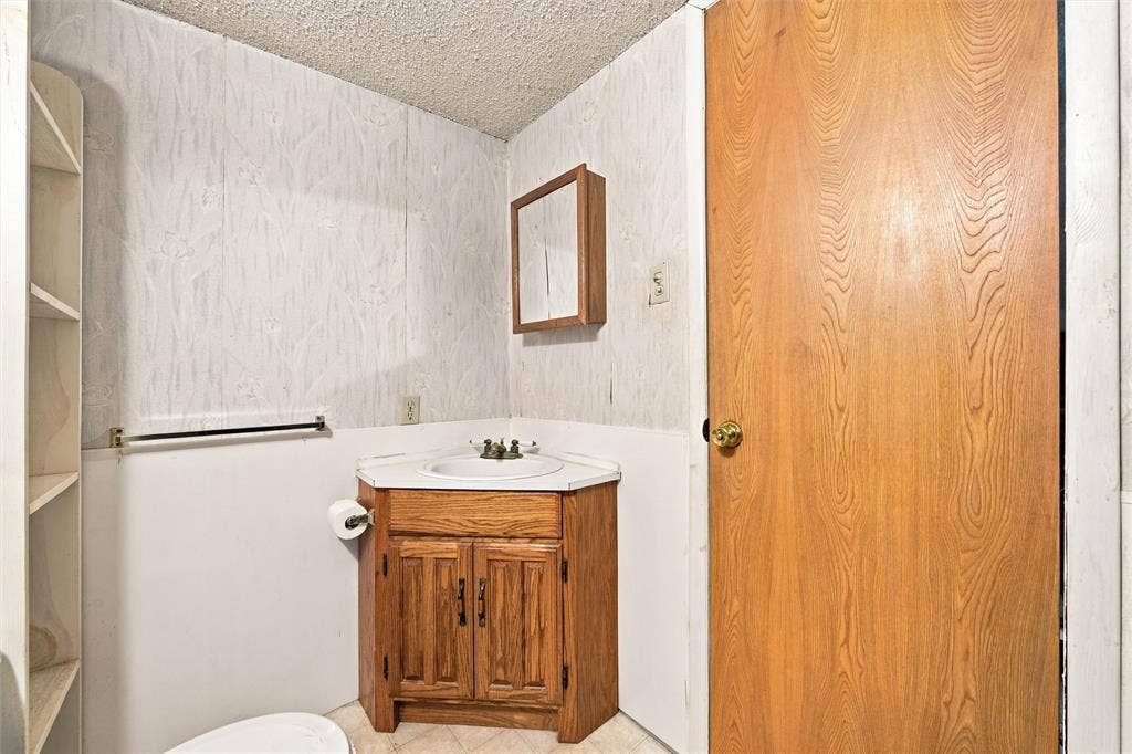 1703 Arra Street, Waco, TX 76704 Corner vanity with wood-finish cabinetry, inset sink, and built-in shelving, complemented by a wall-mounted medicine cabinet and solid wood-finish door