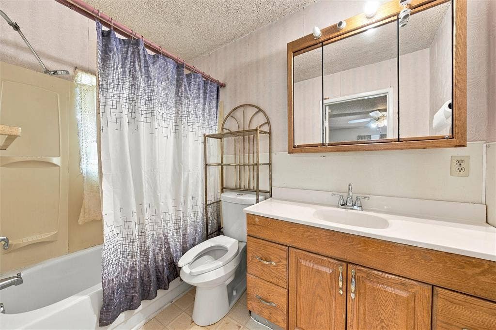 1703 Arra Street, Waco, TX 76704 Bathroom featuring a wood-finish vanity with a molded countertop and integrated sink, a tri-fold medicine cabinet, and a combined tub and shower enclosure with a surround