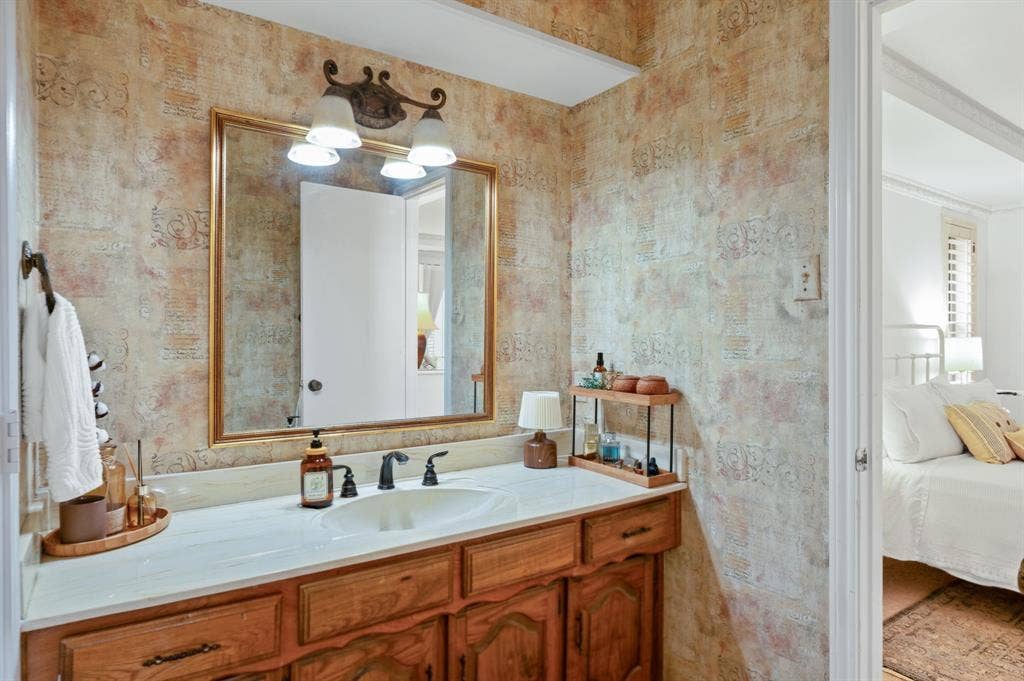 621 Harvest Glen Drive, Richardson, TX 75081 Bathroom vanity featuring a light-toned countertop, an integrated oval sink, three-handle faucet, wood cabinetry, and a large gold-framed mirror with multi-light wall fixture