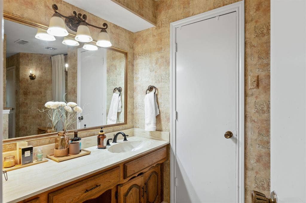 621 Harvest Glen Drive, Richardson, TX 75081 Bathroom vanity featuring a wood cabinet, light-toned countertop, oval undermount sink, and multi-light wall-mounted fixture above a framed mirror