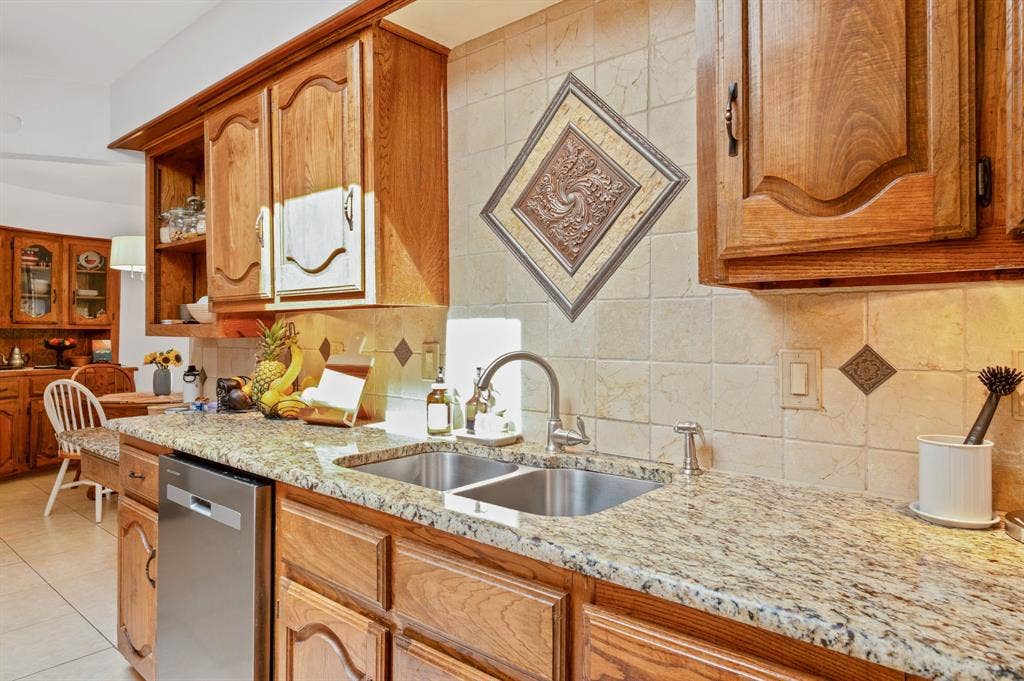 621 Harvest Glen Drive, Richardson, TX 75081 Kitchen featuring wood cabinetry, stone countertops, a dual-basin stainless steel sink with a high-arch faucet, and a decorative tile backsplash