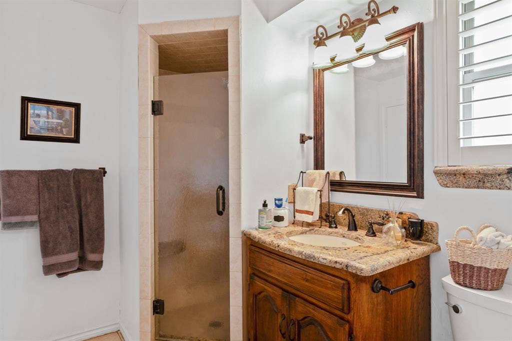 621 Harvest Glen Drive, Richardson, TX 75081 Bathroom featuring a wood vanity with stone countertop, drop-in sink, framed mirror with integrated lighting, and a glass-enclosed shower
