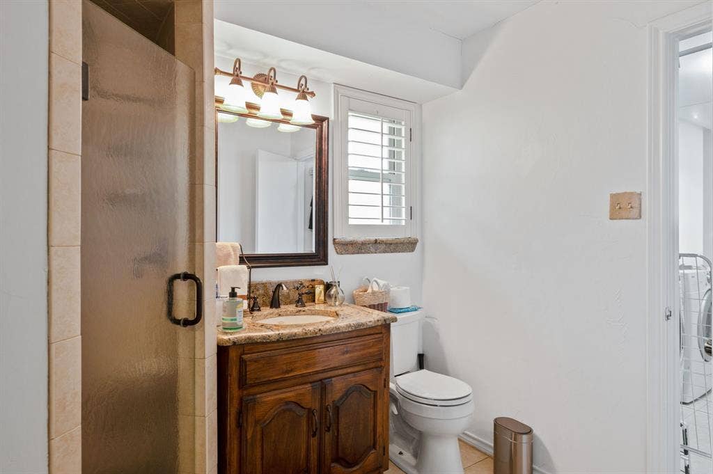 621 Harvest Glen Drive, Richardson, TX 75081 Bathroom featuring a custom wood vanity with a stone countertop, an integrated sink, a framed mirror with a three-light fixture, and a tiled shower stall with a glass door