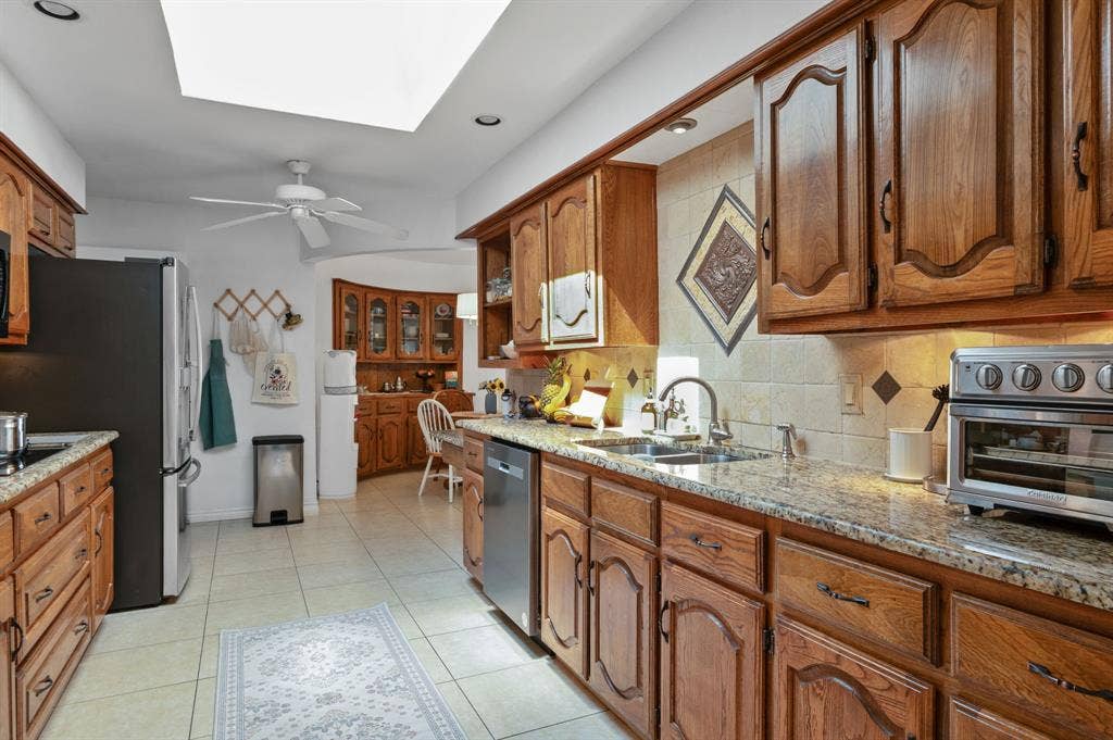 621 Harvest Glen Drive, Richardson, TX 75081 Kitchen featuring wood cabinetry, stone countertops, tiled backsplash with decorative inlay, stainless steel dishwasher, and a skylight