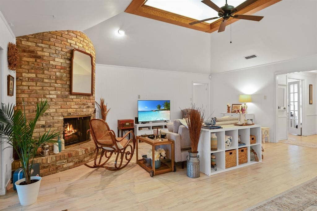 621 Harvest Glen Drive, Richardson, TX 75081 Living area featuring vaulted ceilings, a central skylight with wood trim, a curved brick fireplace, and light-toned wood-finish flooring