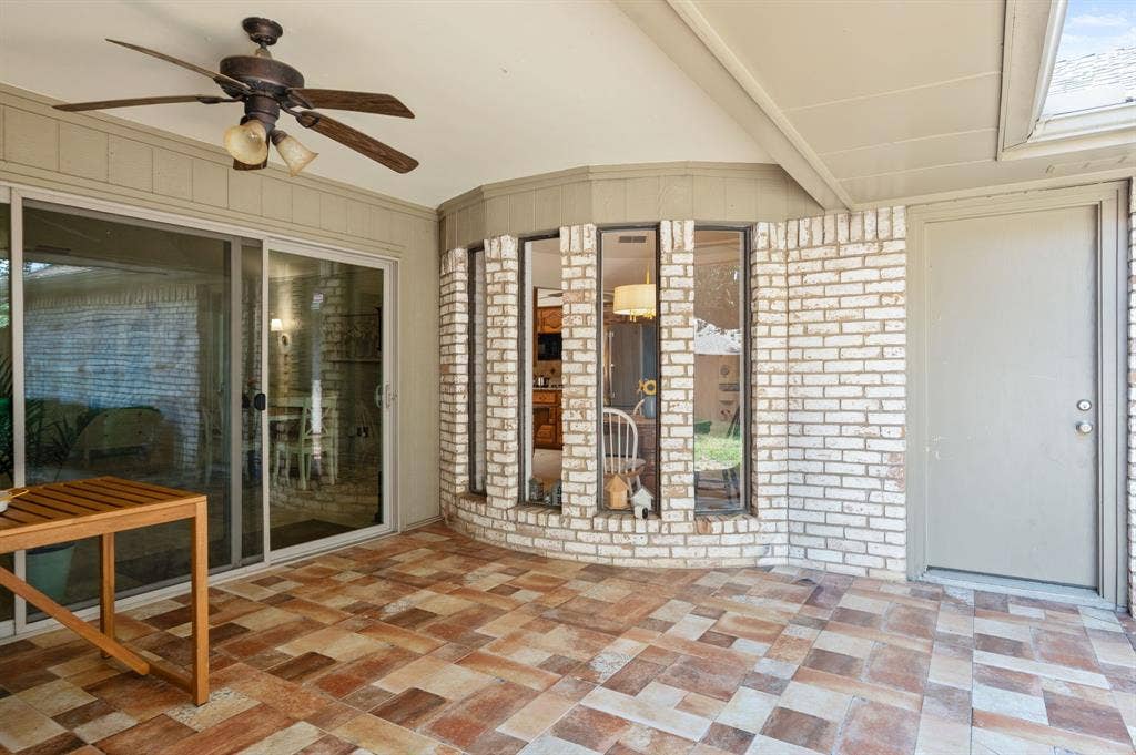 621 Harvest Glen Drive, Richardson, TX 75081 Covered patio featuring a multi-tone tile floor, brick-accented exterior wall, bay window configuration, and a ceiling-mounted fan with integrated lighting