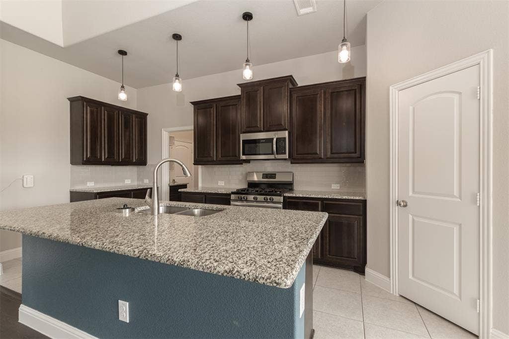 1742 Amalfi Drive, McLendon Chisholm, TX 75032 Kitchen featuring dark wood cabinetry, stone-surface countertops, central island, stainless steel appliances, and pendant lighting