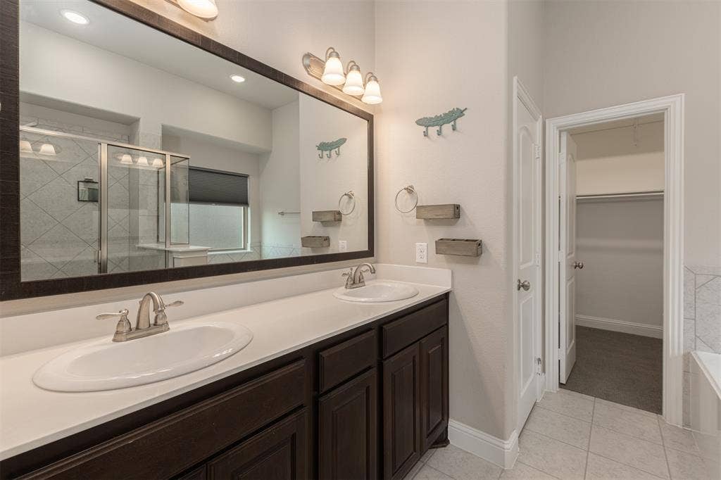 1742 Amalfi Drive, McLendon Chisholm, TX 75032 Dual-sink vanity with dark wood cabinetry, solid-surface countertop, full-width mirror, and integrated lighting