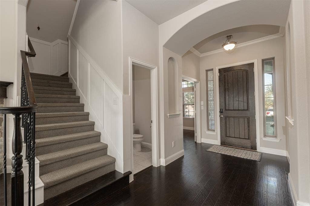 1742 Amalfi Drive, McLendon Chisholm, TX 75032 Foyer featuring a dark-finish wooden door with glass sidelights, an arched entryway, dark wood-finish flooring, and a staircase with carpeted treads and an iron baluster