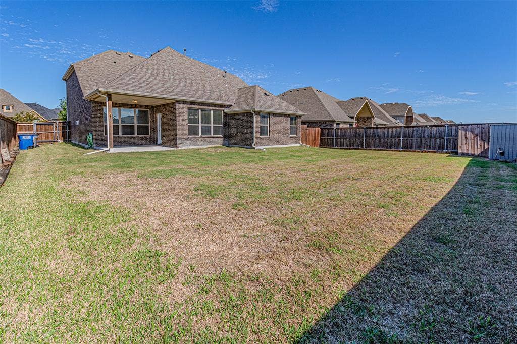 1742 Amalfi Drive, McLendon Chisholm, TX 75032 Brick exterior featuring a covered rear patio, expansive lawn, and full wood privacy fencing